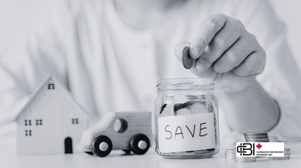 Hand placing a coin into a savings jar labeled "Save" beside a toy house and car, representing saving money on home and auto insurance.