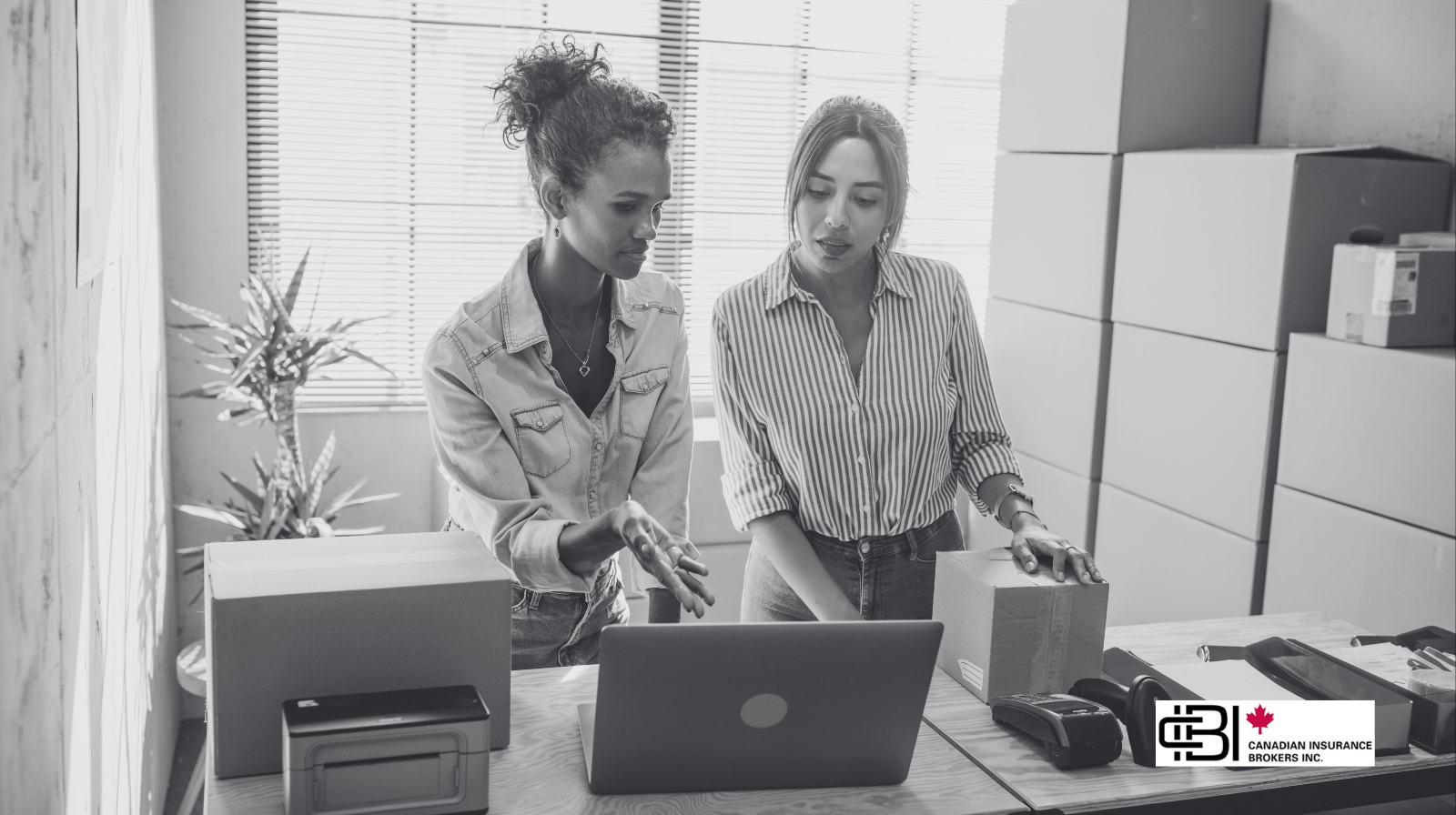 Two small business owners reviewing orders on a laptop while packing boxes in a home workspace and discussing small business insurance in oakville